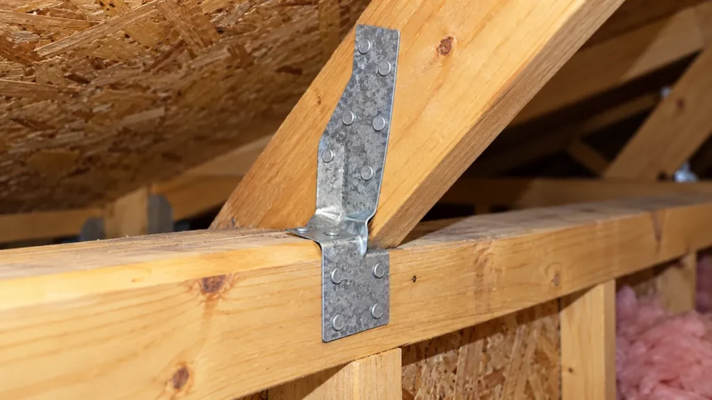 Metal hurricane straps connecting roof trusses to the top of a wall in an attic